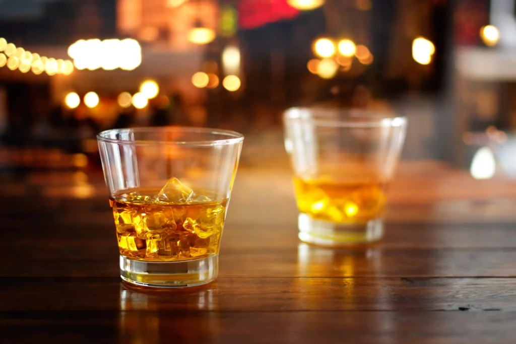 Two full shot glasses sitting on a bar counter.